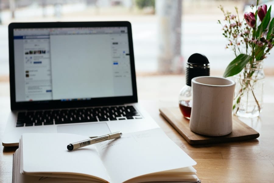 Imagem mostra um laptop aberto, com um caderno acima dele / Foto: Nick Morrison/Unsplash
